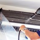 The technicians are cleaning the air conditioner by spraying water. Hand and water spray are cleaning the air conditioner on white background.